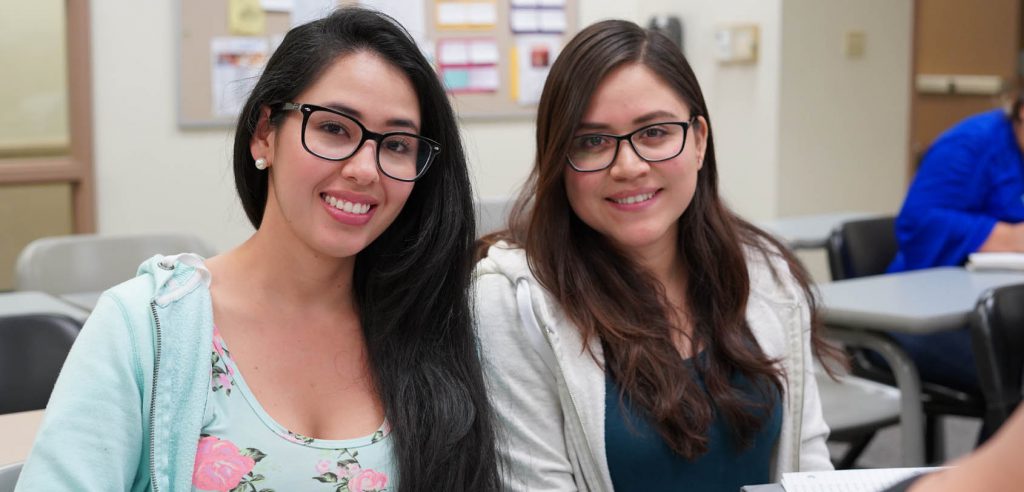 two smiling young women sitting together in class