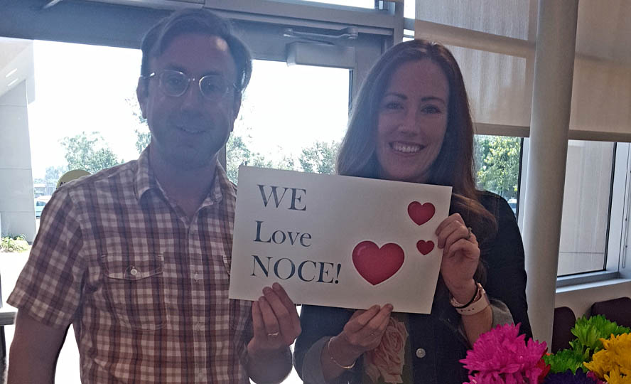 A photo of two DSS counselors holding a "We Love NOCE" sign. 