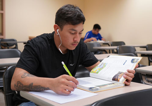 A photo of a student working on an assigment as, while he reads his textbook