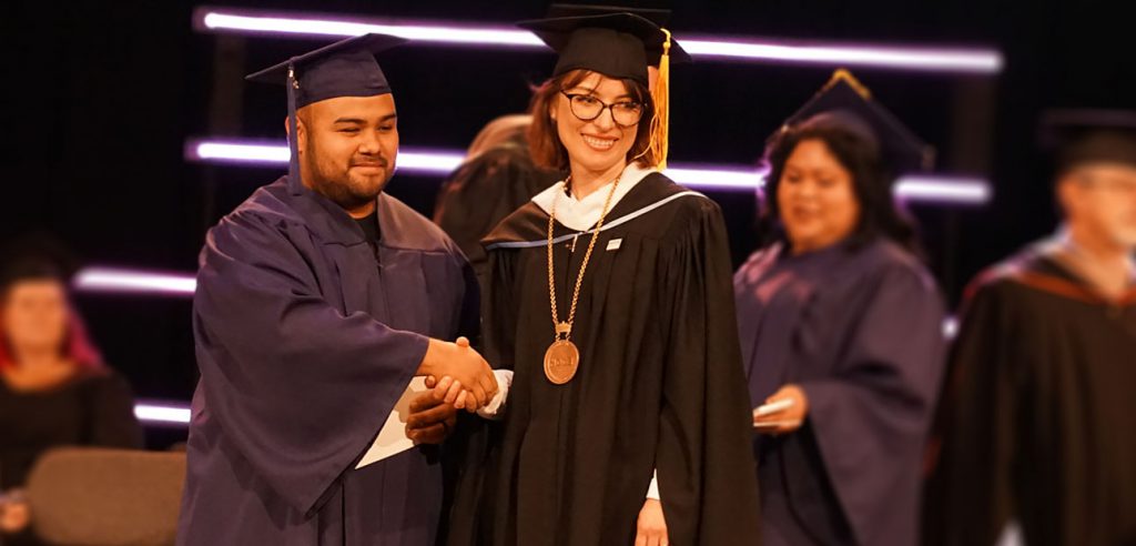 A photo of NOCE President Valentina Purtell shaking hands with a student during the commencemnt ceremony
