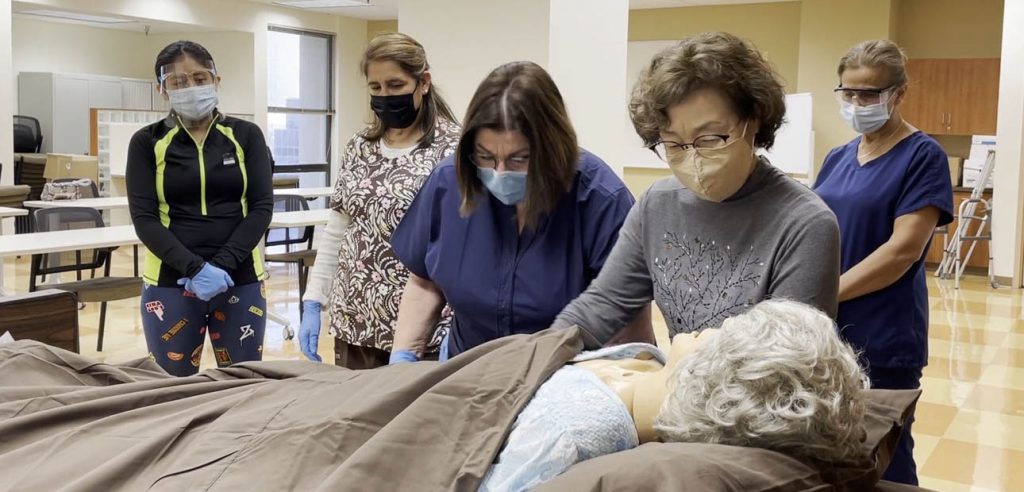 NOCE personal care aide students learning how to move a patient in bed. 