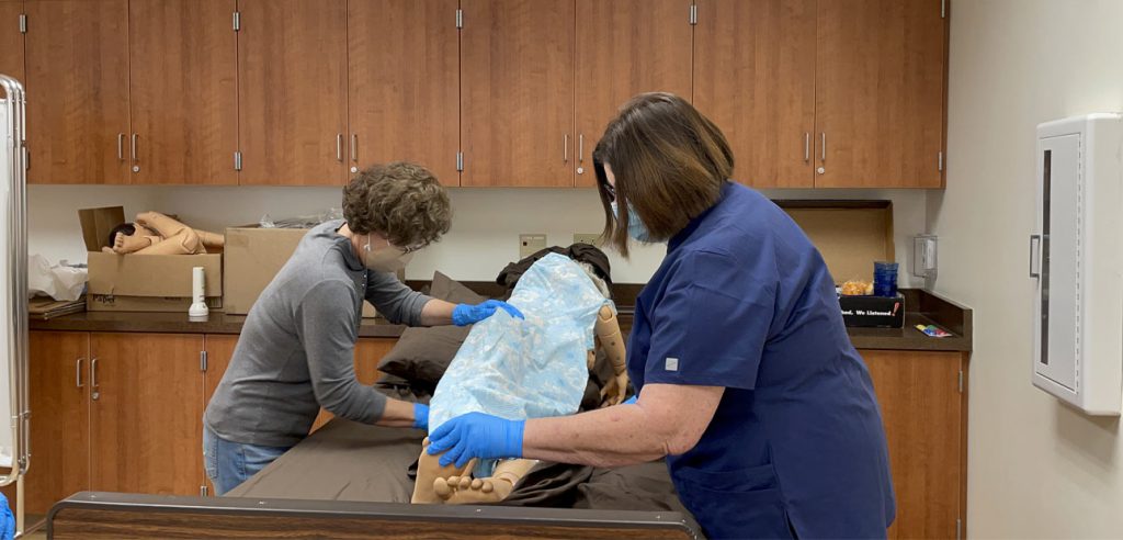 two students in the personal care aide class, learning to change bedsheets while a patient is still in bed