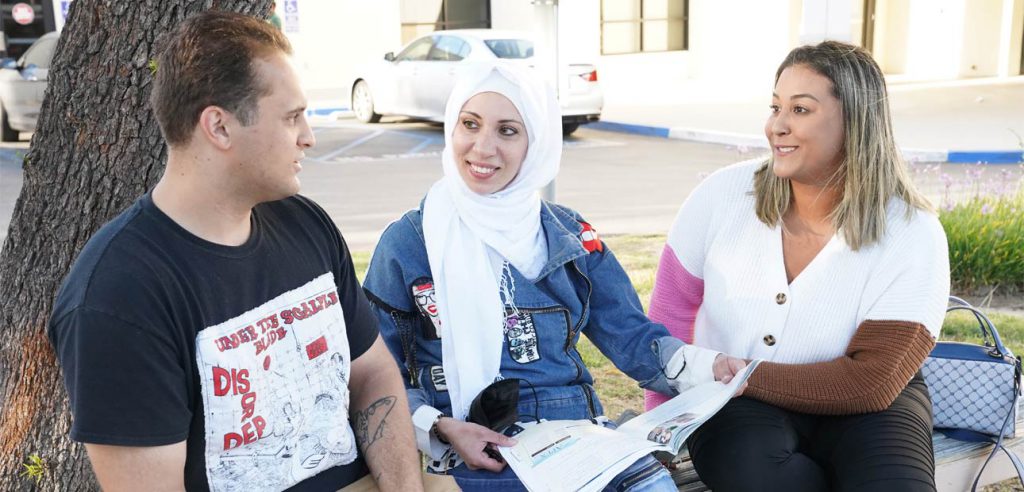 A male student, and two female students talking outside the entrance of the Anaheim Campus