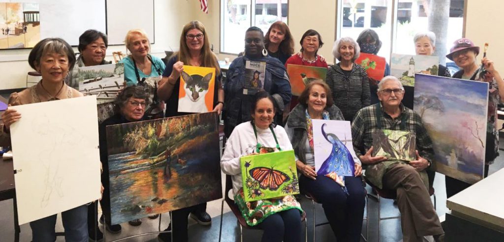 A group photo of the Older Adults' Painting class with everyone posing with their paintings.