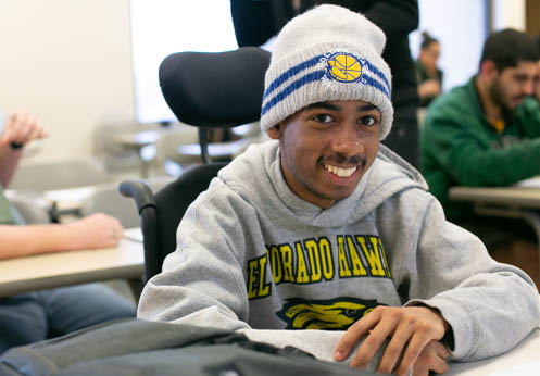 Un estudiante negro sonriente sentado en su silla de ruedas en su escritorio.