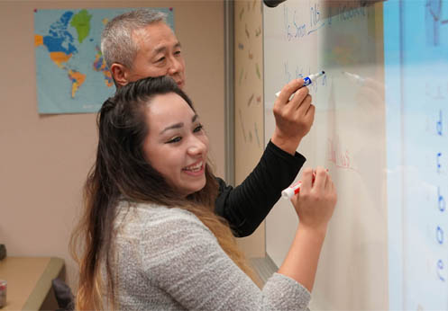 Two ESL students writing on the whiteboard in class.