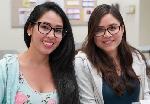 Two smiling young women sitting together in class