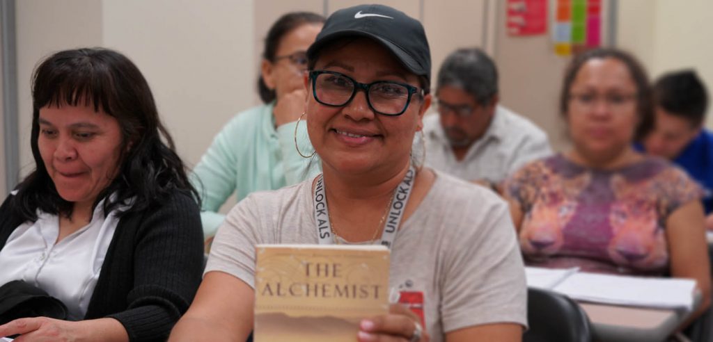 A photo NOCE ESL student holding up a book titled “The Alchemist”