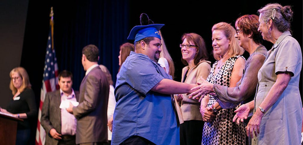 Man graduating from NOCE's program for adults with disabilities shakes the hands of NOCE faculty