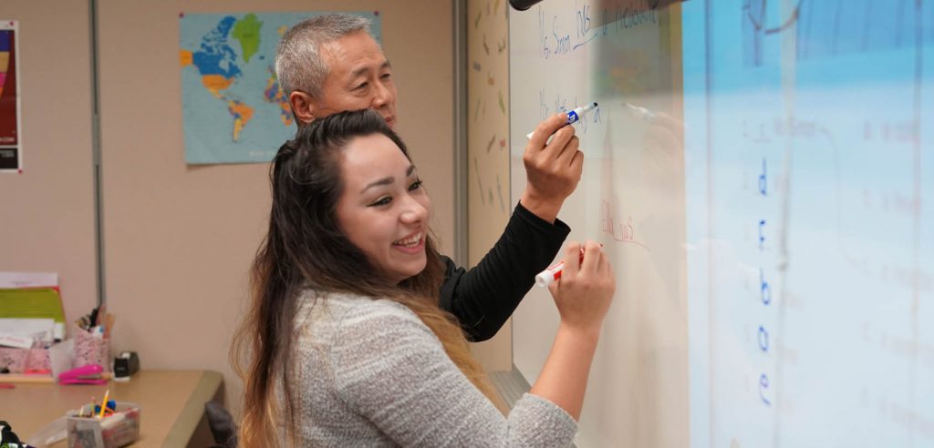 A photo of two ESL students writing on the whiteboard in class.