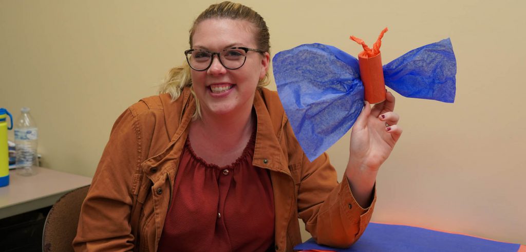 A photo of a smiling NOCE student holding up her paper mache butterfly.