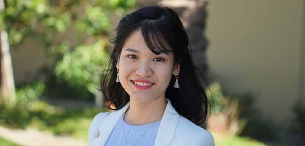 An Asian woman smiling in a white blazer and light blue blouse.