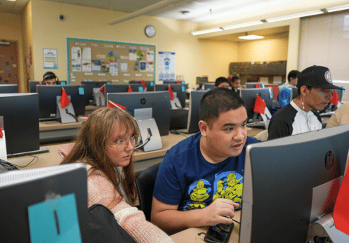 DSS students in an advanced computer class. A female teacher is assisting a male student.