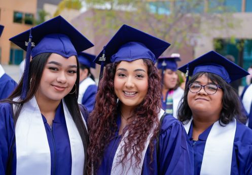 Three CTE graduate students in their blue caps and gowns and a white sash.