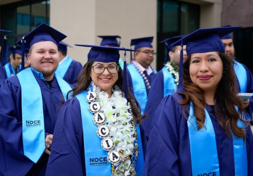 Three DSS graduate students in their blue caps and gowns and a light blue sash.