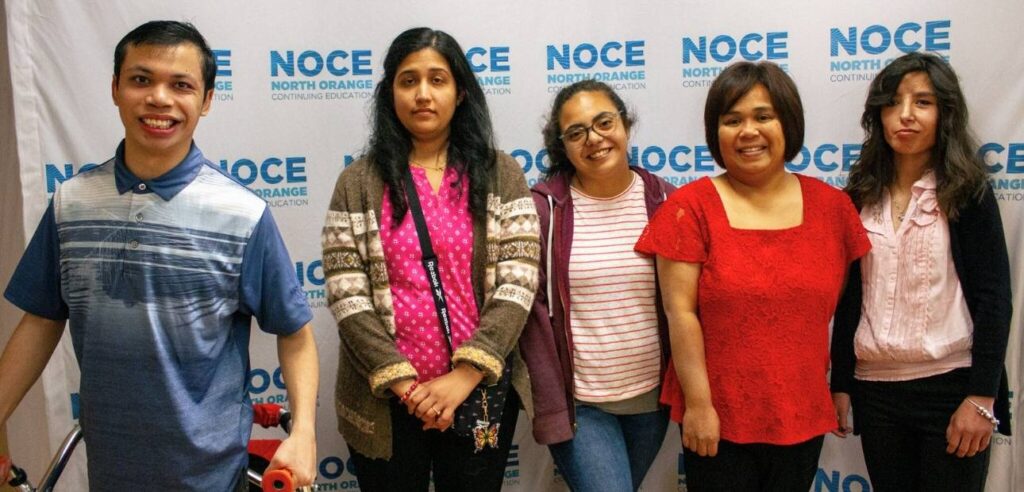 4 female and 1 male students posing for a photo in front of the NOCE background