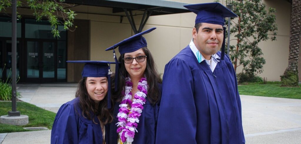 3 graduating students posing for a photo in their dark blue robe and cap.