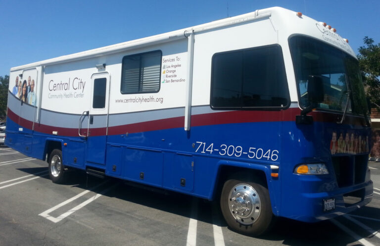 A large white, grey, blue and red RV that has been modified by Central City Community Health Center as a mobile health clinic