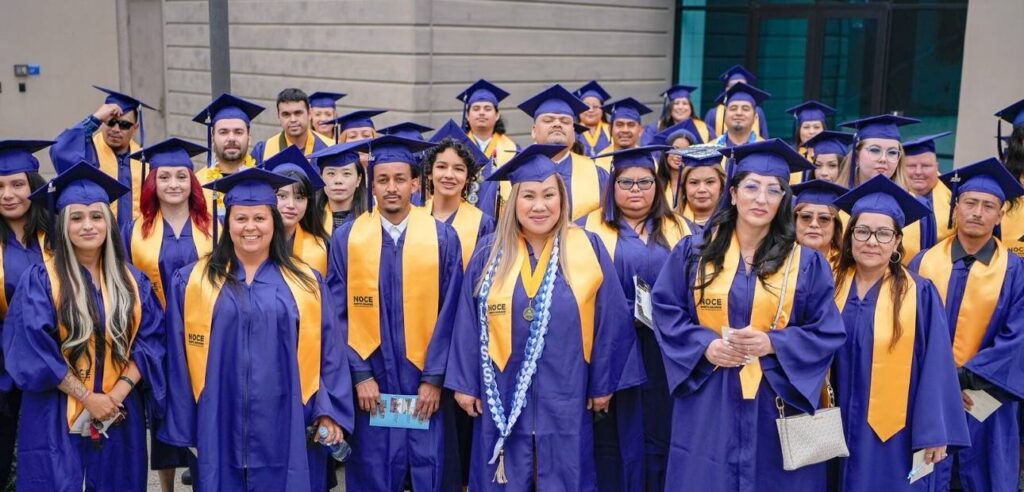 A group photo of the high school diploma program graduates. They are all wearing dark blue cap and grown with a gold yellow NOCE sash.