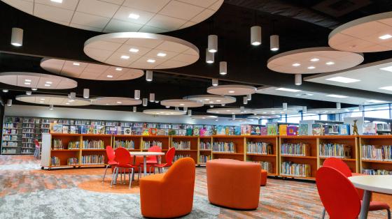 The Cypress Library with a half bookshelves with lots of books. There are white tables and orange chairs for people to sit and enjoy.