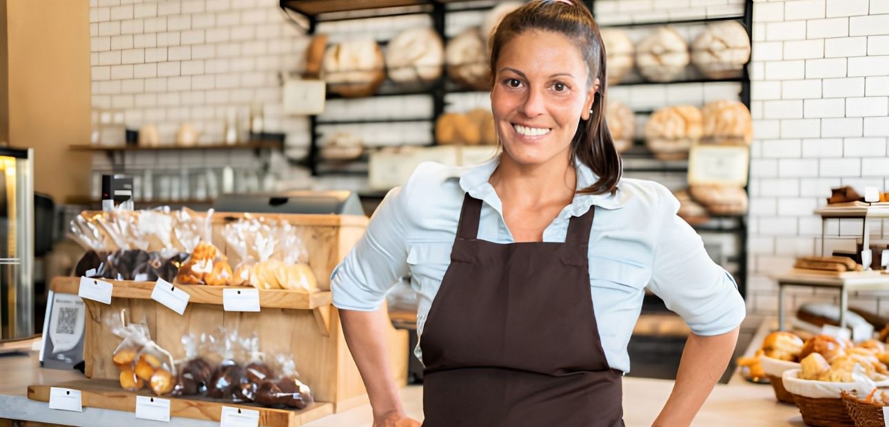 Confident smiling small coffee shop owner standing at the counter. Woman wearing apron standing in bakery and looking at camera.