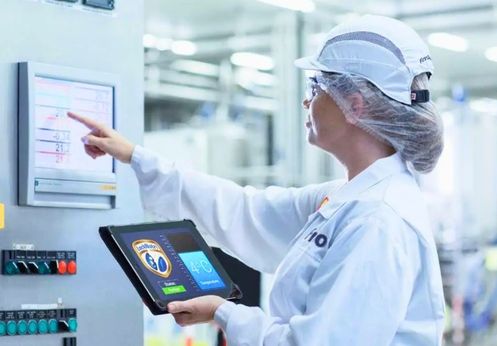 Quality assurance technician monitoring medical device manufacturing process using tablet and control panel display