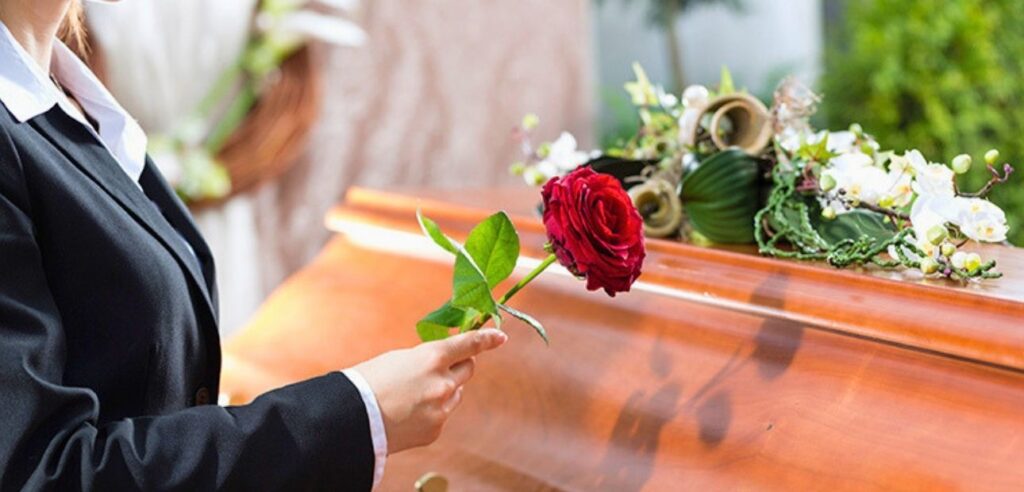 Woman holding a red rose next to a casket at a funeral service.