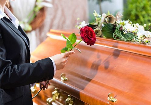 Woman holding a red rose next to a casket at a funeral service.