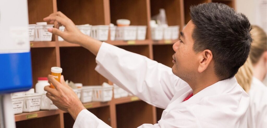 Pharmacy technician selecting medication bottle from organized shelving unit in clinical pharmacy setting