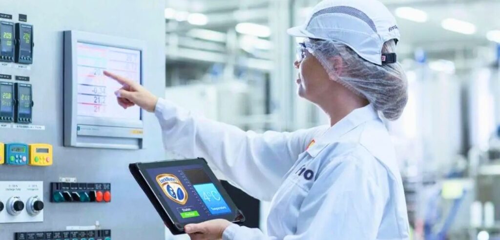 Quality assurance technician monitoring medical device manufacturing process using tablet and control panel display