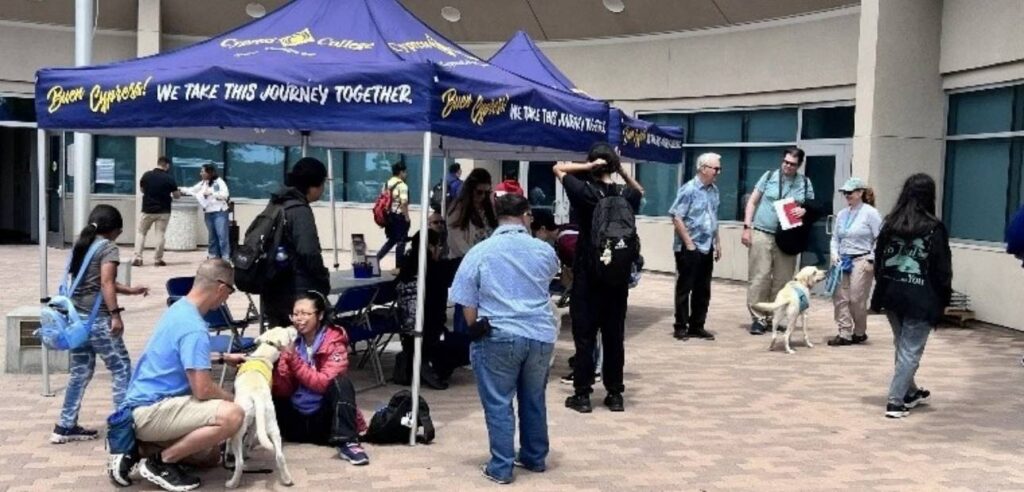 People gather outside under blue Cypress College tents